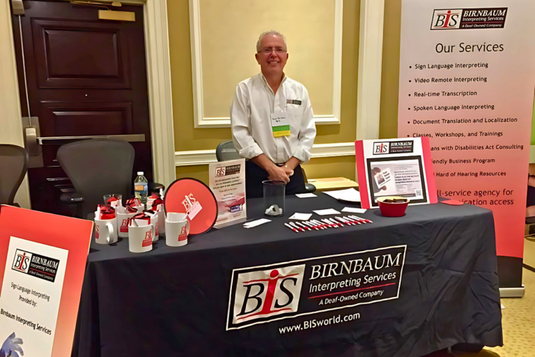 David Birnbaum standing behind a Birnbaum Interpreting Services table at a trade show