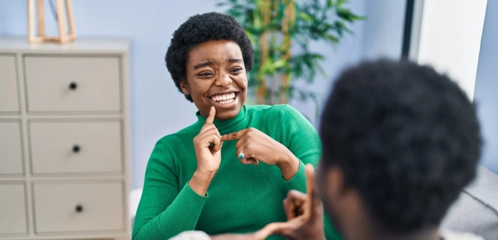 Women in green sweater, smiling while conversing to her friend in American Sign Language (ASL)